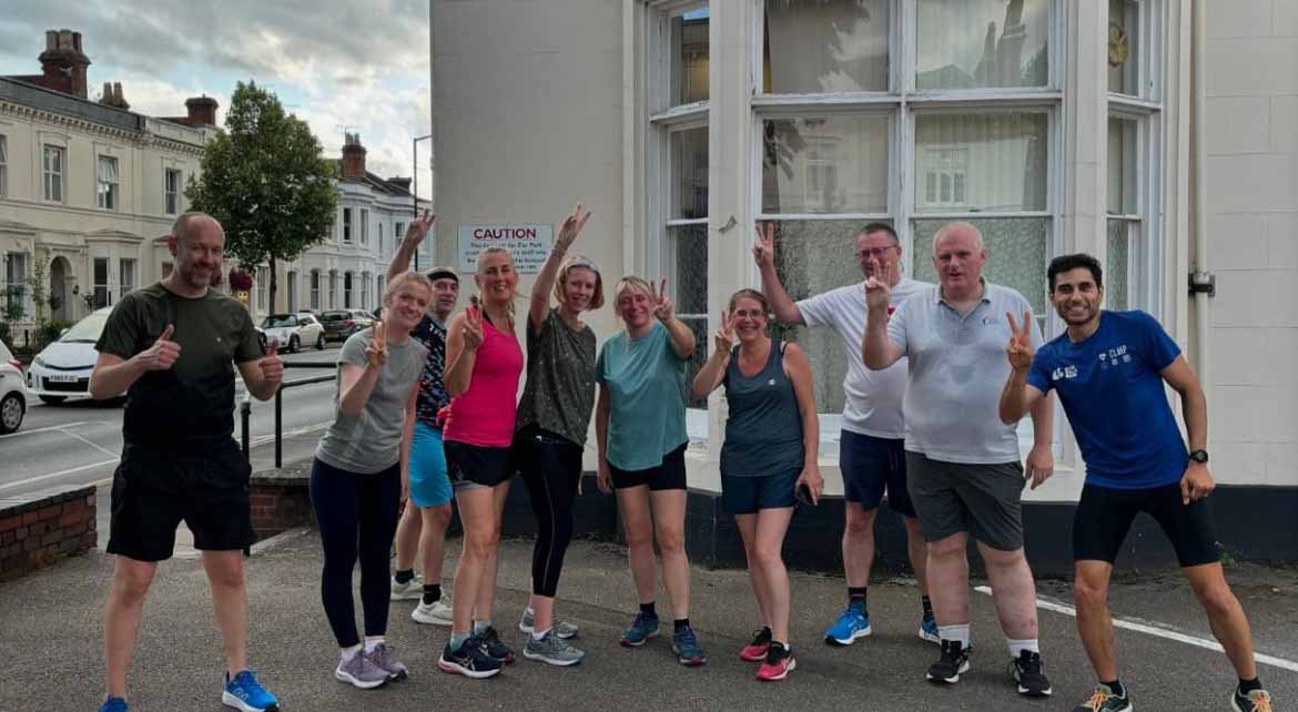 Toni with her staff at the GP standing outside the surgery in running gear with their hands up doing a peace sign