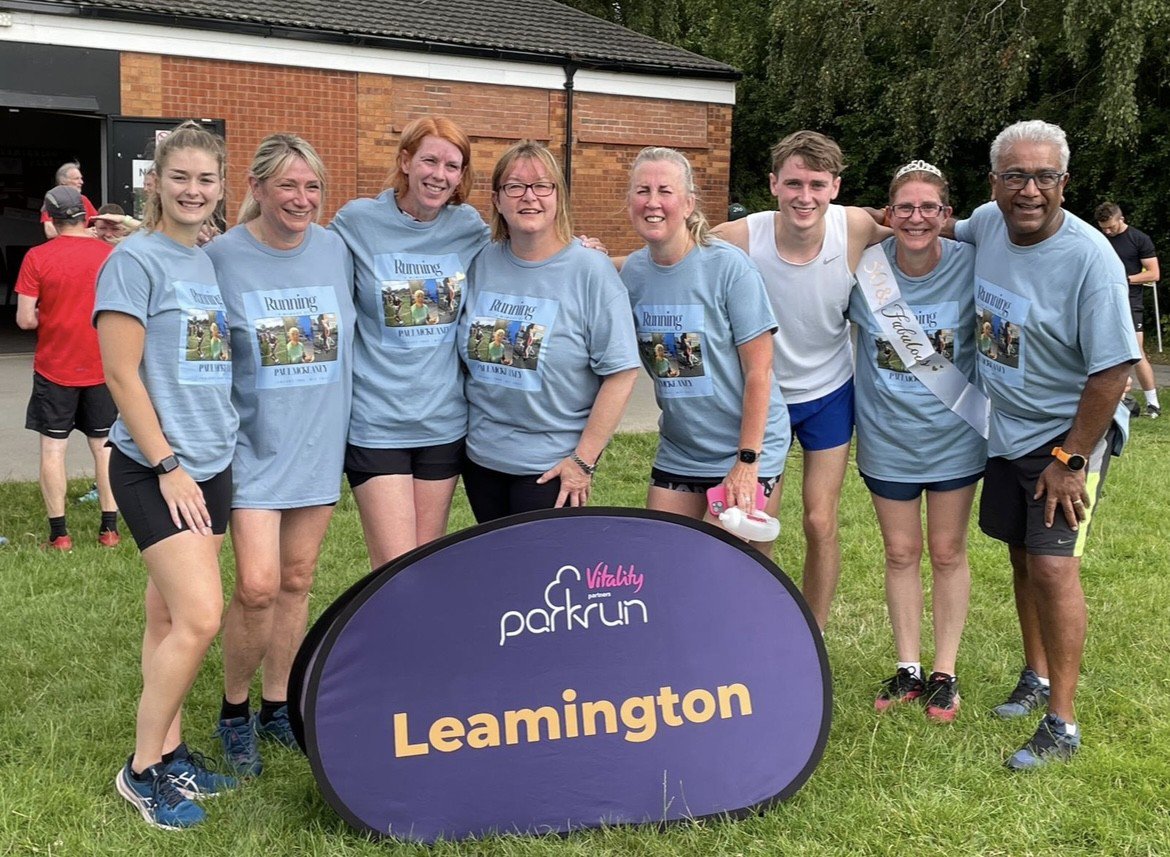 Toni at a park run with friends and family, standing in front of a sign that reads 'parkrun leamington'